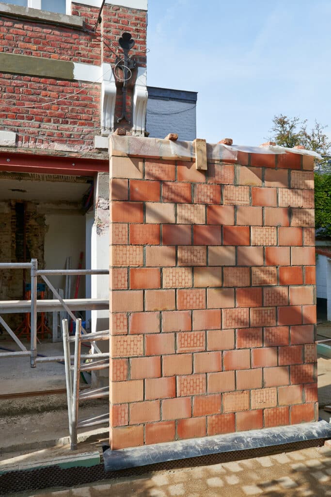 Rénovation maison: façade ancienne en briques, nouveau mur en briques apparentes en construction. Poutre métallique, échafaudage et fondations.